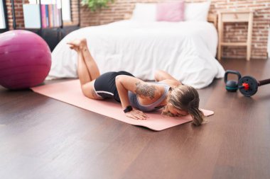 Genç sarışın kadın yatak odasında yoga egzersizi yapıyor.