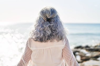 Orta yaşlı bir kadın deniz kenarında arka planda duruyor.