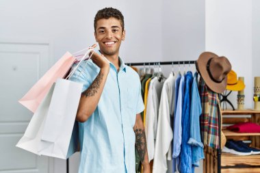 Perakende dükkanında alışveriş torbaları tutan gülümseyen İspanyol genç adam.