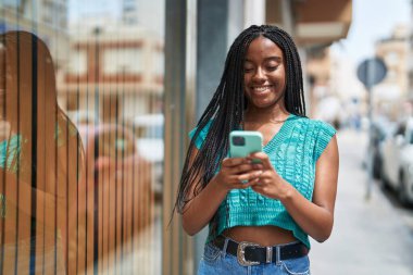 Afro-Amerikalı kadın sokakta akıllı telefon kullanarak kendine güveniyor.