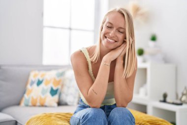 Sarışın genç bir kadın evdeki koltukta kendinden emin bir şekilde oturarak gülümsüyor.