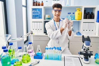 Laboratuvarda test tüpünde yazan bilim adamı üniforması giyen İspanyol genç adam.