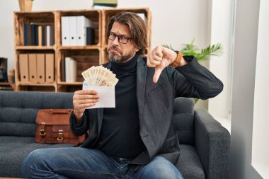 Muayenehanedeki yakışıklı orta yaşlı adam elinde kızgın yüzüyle dkk banknotları tutuyor. Eksi işareti baş parmakları aşağıda, reddedilme konsepti ise olumsuz. 