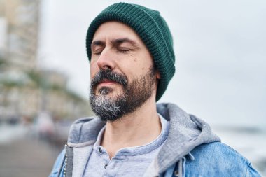 Genç kel adam deniz kenarında gözleri kapalı nefes alıyor.