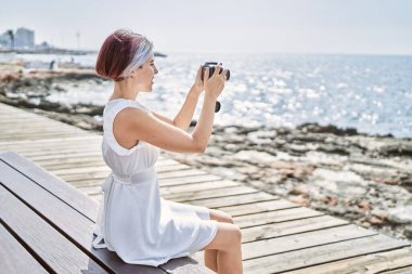 Sahildeki bankta oturan beyaz bir kız profesyonel kamera kullanıyor..
