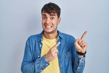 Mavi arka planda dikilen Latin asıllı genç adam iki eliyle endişeli ve gergin bir ifadeye işaret ediyor. 