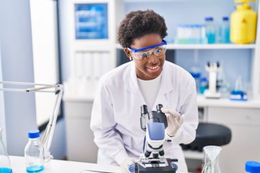 Laboratuvarda mikroskop kullanarak bilim adamı üniforması giyen Afrikalı Amerikalı bir kadın.