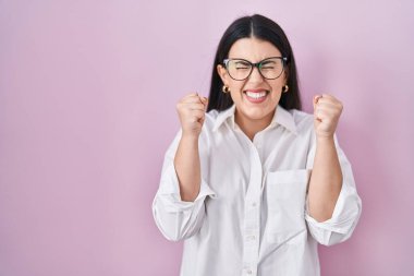 Pembe arka planda duran genç esmer kadın başarı için heyecanlı kolları havada ve gözleri kapalı zaferi kutlarken gülümsüyor. Kazanan konsept. 