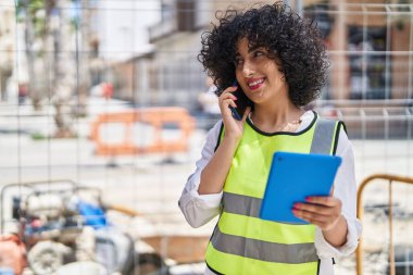 Young middle east woman architect talking on smartphone using touchpad at street