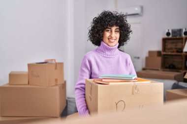 Young middle east woman smiling confident holding books package at new home