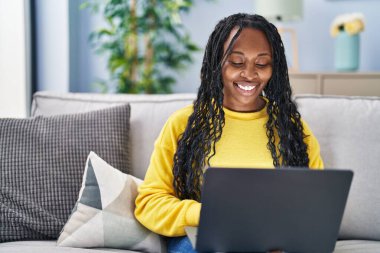 African american woman using laptop sitting on sofa at home