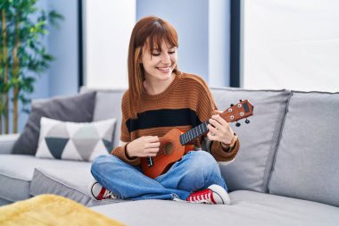 Evdeki koltukta ukelele oynayan genç bir kadın.