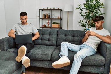 Evde akıllı telefon ve dizüstü bilgisayar kullanan iki İspanyol erkek.
