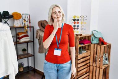 Perakende mağazasında yönetici olarak çalışan beyaz bir kadın diş ağrısı ya da diş ağrısı yüzünden ağızlarına acı dolu bir ifadeyle dokunuyor. dişçi 