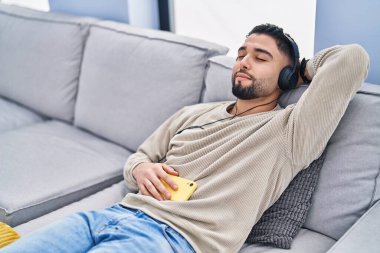 Genç Arap adam evdeki kanepede müzik dinliyor.