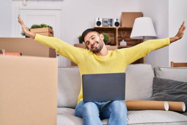 Genç İspanyol adam yeni evinde dizüstü bilgisayar kullanıyor.