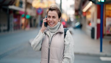 Orta yaşlı İspanyol kadın gülümsüyor. Akıllı telefondan konuşuyor.