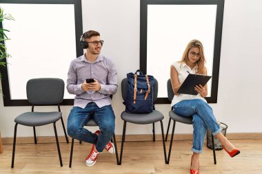 İki İspanyol mutlu bir şekilde gülümsüyor. Bekleme odasında akıllı telefon kullanıyor.