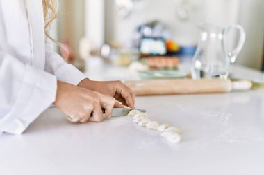 Young woman wearing cook uniform cutting dough at kitchen