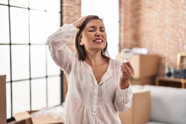 Orta yaşlı İspanyol bir kadın elinde ilham ve fikir için ampul tutuyor. Kafası karışık, şaşırmış ve kızgın bir yüz. 