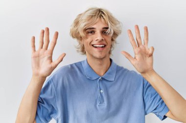 İzole edilmiş arka planda duran genç ve modern bir adam dokuz numarayı gösterip işaret ederken kendinden emin ve mutlu gülümsüyor.. 
