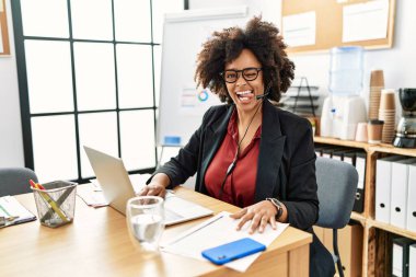 Ofiste çalışan afro saçlı Afro-Amerikalı kadın operatör kulaklığı takıyor ve komik bir ifadeyle dilini dışarı çıkarıyor. duygu kavramı. 