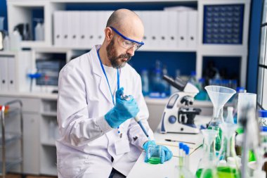 Genç kel bilim adamı laboratuarda test tüpüne sıvı döküyor.