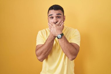 Sarı arka planda duran İspanyol genç adam yanlışlıkla ağzı ellerle kapatarak şok geçirdi. gizli kavram. 