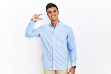 İzole edilmiş arka planda duran İspanyol gömlekli genç adam gülümsüyor ve el hareketleriyle küçük boy işaretler yaparak kameraya bakıyor. ölçüm kavramı. 