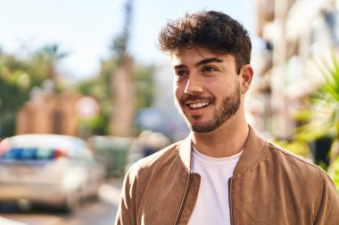 Young hispanic man smiling confident looking to the side at street