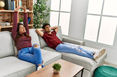 Genç Latin çift esnemekten ve kollarını esnetmekten yoruldu. Evdeki kanepede oturuyorlar..