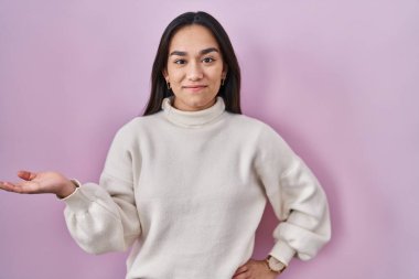 Pembe arka planda duran genç Güney Asyalı kadın mutlu bir şekilde sunum yapıyor ve avuç içi kameraya bakıyor.. 