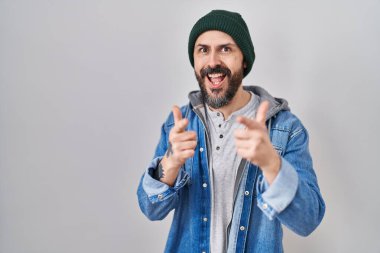 Dövmeli, yün şapkalı, mutlu ve komik yüzlü, kameraya işaret eden genç İspanyol bir adam. iyi enerji ve titreşimler. 