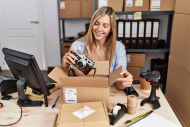 Young blonde woman ecommerce business worker packing vintage camera on order package at office