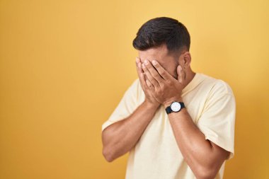 Sarı arka planda dikilen yakışıklı İspanyol adam. Ağlarken suratını ellerle kapatıyor. depresyon kavramı. 