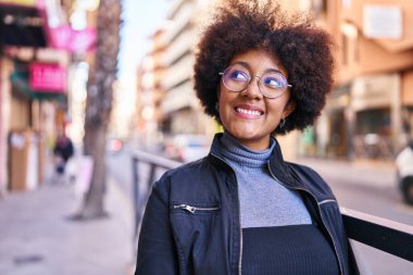 Afro-Amerikalı kadın gülümsüyor. Kendinden emin bir şekilde caddeye bakıyor.