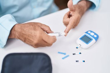 Senior grey-haired man measuring glucose sitting on table at home