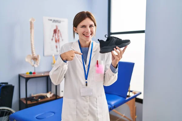 Joven Fisioterapeuta Mujer Sosteniendo Zapatillas Deporte Señalando Dedo Uno Mismo —  Fotos de Stock