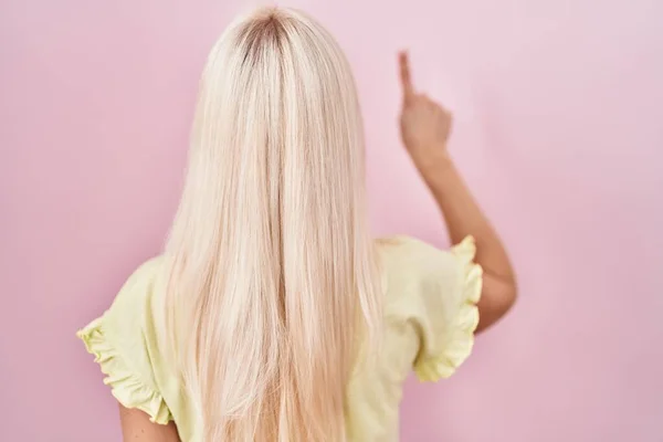 Kaukasische Frau Vor Rosa Hintergrund Posiert Rückwärts Und Zeigt Mit — Stockfoto