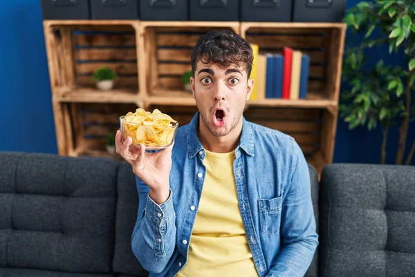 Ung Latinamerikansk Man Håller Potatischips Rädd Och Förvånad Med Öppen — Stockfoto