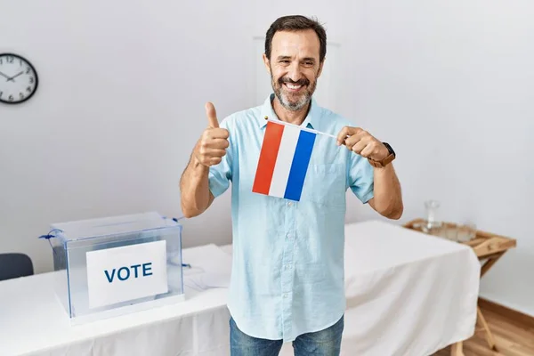 政治選挙で髭を生やした中年の男がオランダ国旗を掲げて笑顔で肯定的で 親指を上げて優れた承認サインをする — ストック写真
