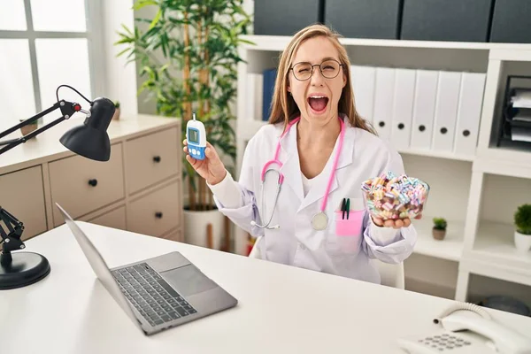 Young Blonde Doctor Woman Holding Glucometer Sweets Winking Looking Camera — Stock Photo, Image