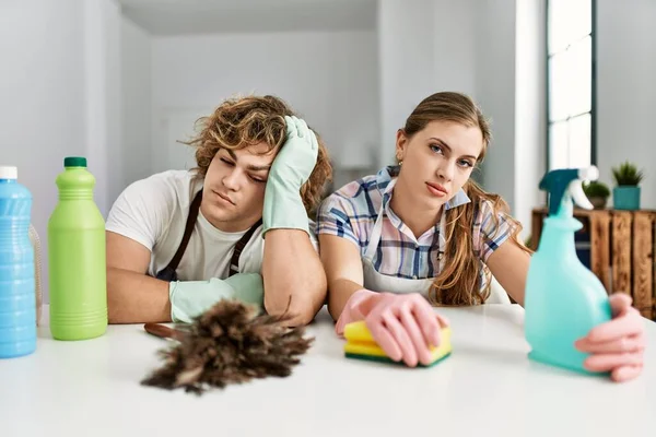 Young caucasian couple exhausted cleaning house sitting on the table.