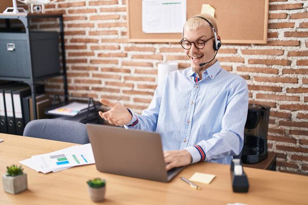 Молодой кавказский мужчина в наушниках агента колл-центра празднует достижение со счастливой улыбкой и выражением победителя с поднятой рукой 