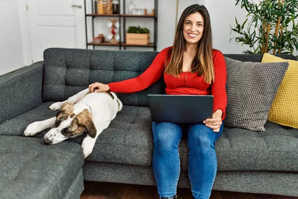 若いです女性使用してノートパソコン上のソファに座って犬とともに自宅 — ストック写真