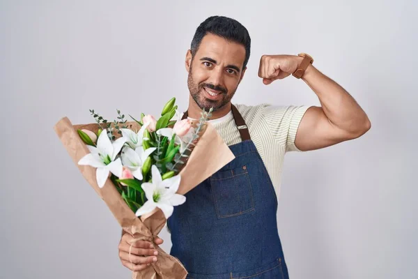Hispanic man with beard working as florist strong person showing arm muscle, confident and proud of power