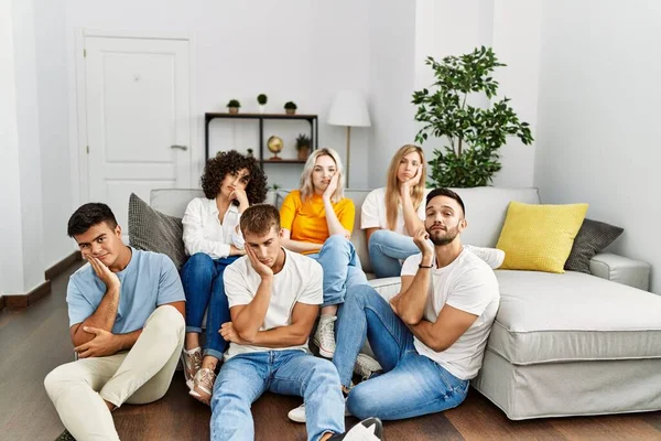 Group of people sitting on the sofa and floor at home thinking looking tired and bored with depression problems with crossed arms.