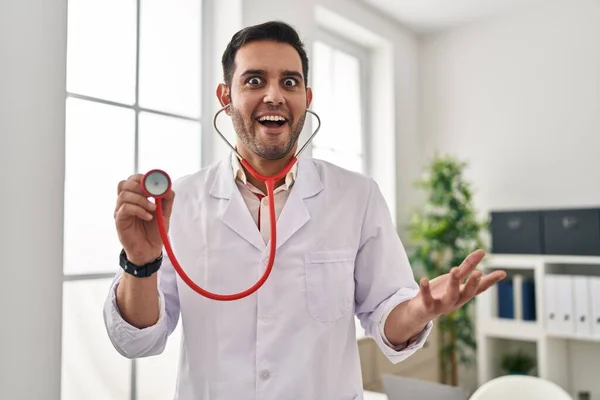 Joven Médico Hispano Con Barba Sosteniendo Estetoscopio Auscultando Celebrando Loco —  Fotos de Stock