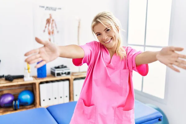 年轻的高加索女人在疼痛恢复诊所工作 看着相机 张开双臂拥抱 欢快的表达拥抱幸福 — 图库照片