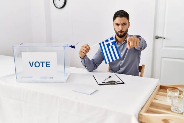 政治選挙で髭を生やした若いハンサムな男は カメラとあなたに指で指差すギリシャの旗を持っています — ストック写真